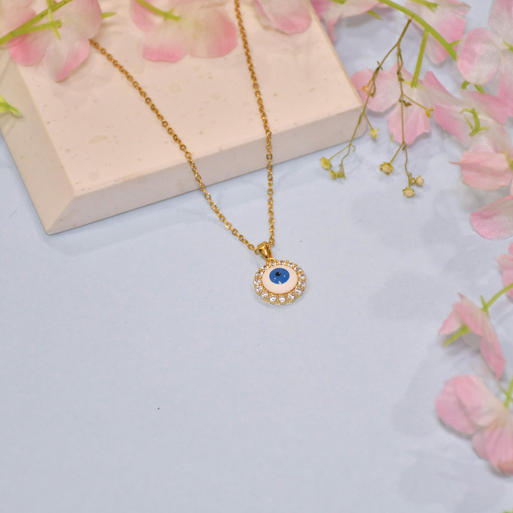 Gold necklace with a blue stone pendant on a light blue background with pink flowers.