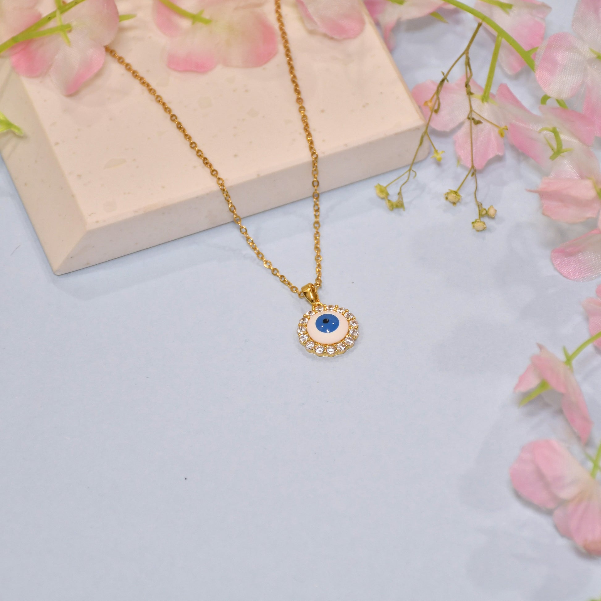 Gold necklace with a blue stone pendant on a light blue background with pink flowers.
