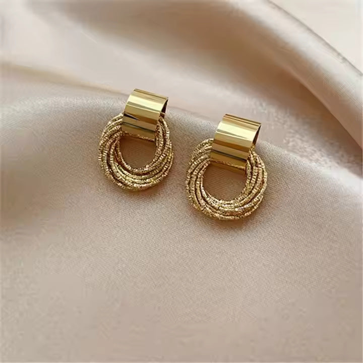 Pair of gold hoop earrings on a beige fabric background